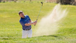 A golfer hitting a bunker shot at Essendon Golf Club