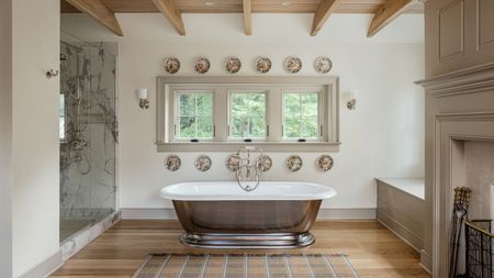 Stunning opulent bathroom with wooden floors, dark veined marble walk in shower, steels free standing bath, plates on walls and beamed ceilings, plus a fireplace in neutral colors