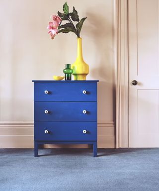 A blue set of drawers in a pink room with a blue carpet