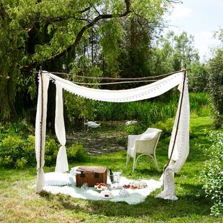 Large garden with canopy, white wicker chair and picnic blanket