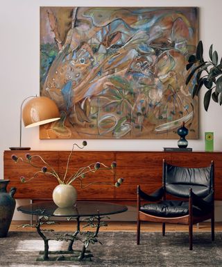 A large wooden console table with a black leather chair and a large piece of abstract artwork hanging behind