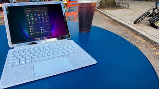 Surface Go 3 on a blue table outdoors next to a cup of iced coffee