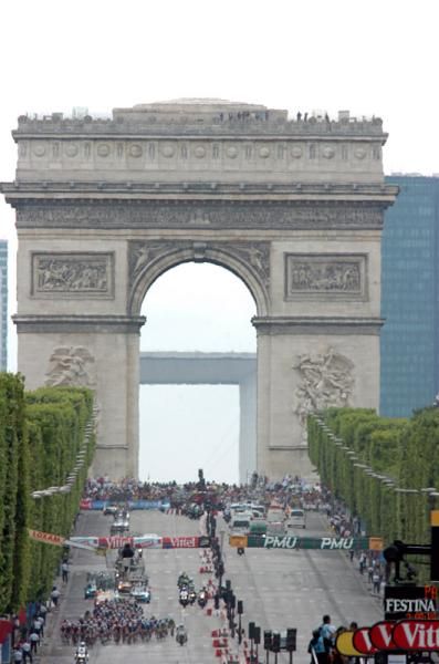 The peloton is dwarfed by the Arc de Triomphe.
