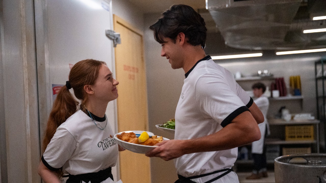 पर्सी आणि सॅम रेस्टॉरंटच्या मागे उभे असताना एकमेकांकडे हसत आहेत. सॅमने जेवणाच्या दोन प्लेट्स धरल्या आहेत.