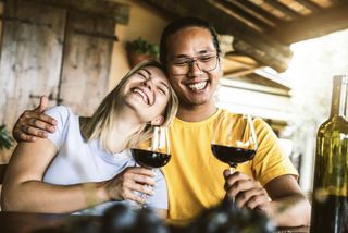 A couple are smiling and enjoying a glass of red wine together.