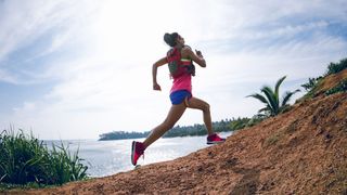 En kvinna i träningskläder som springer uppför en backe bredvid en kustlinje.