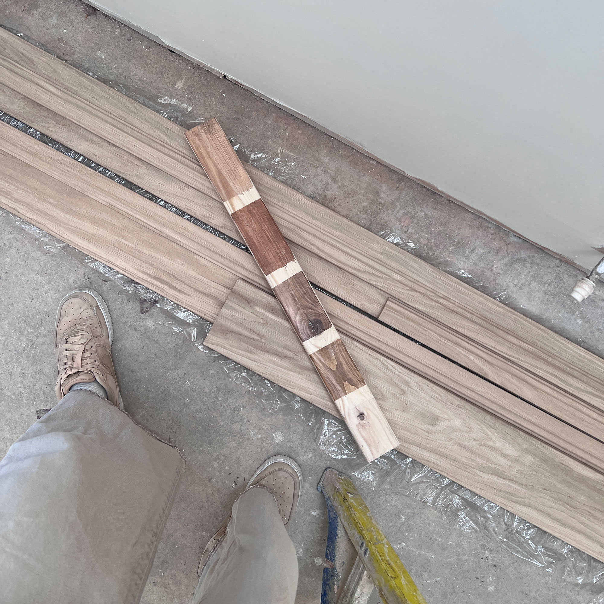Planks of wood on floor, topped with one plank showing effects of various stains