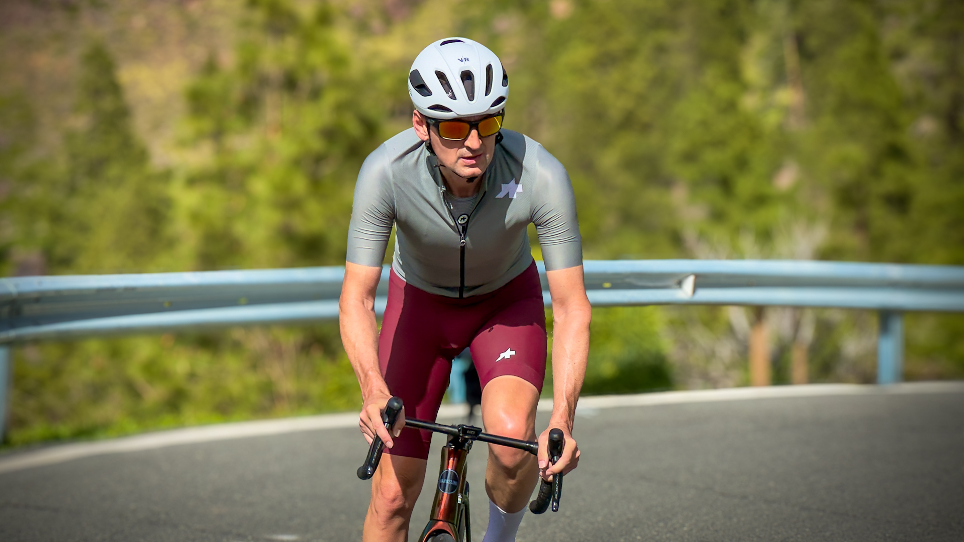 Man wearing green jersey, red shorts and white helmet riding out of the saddle towards the camera
