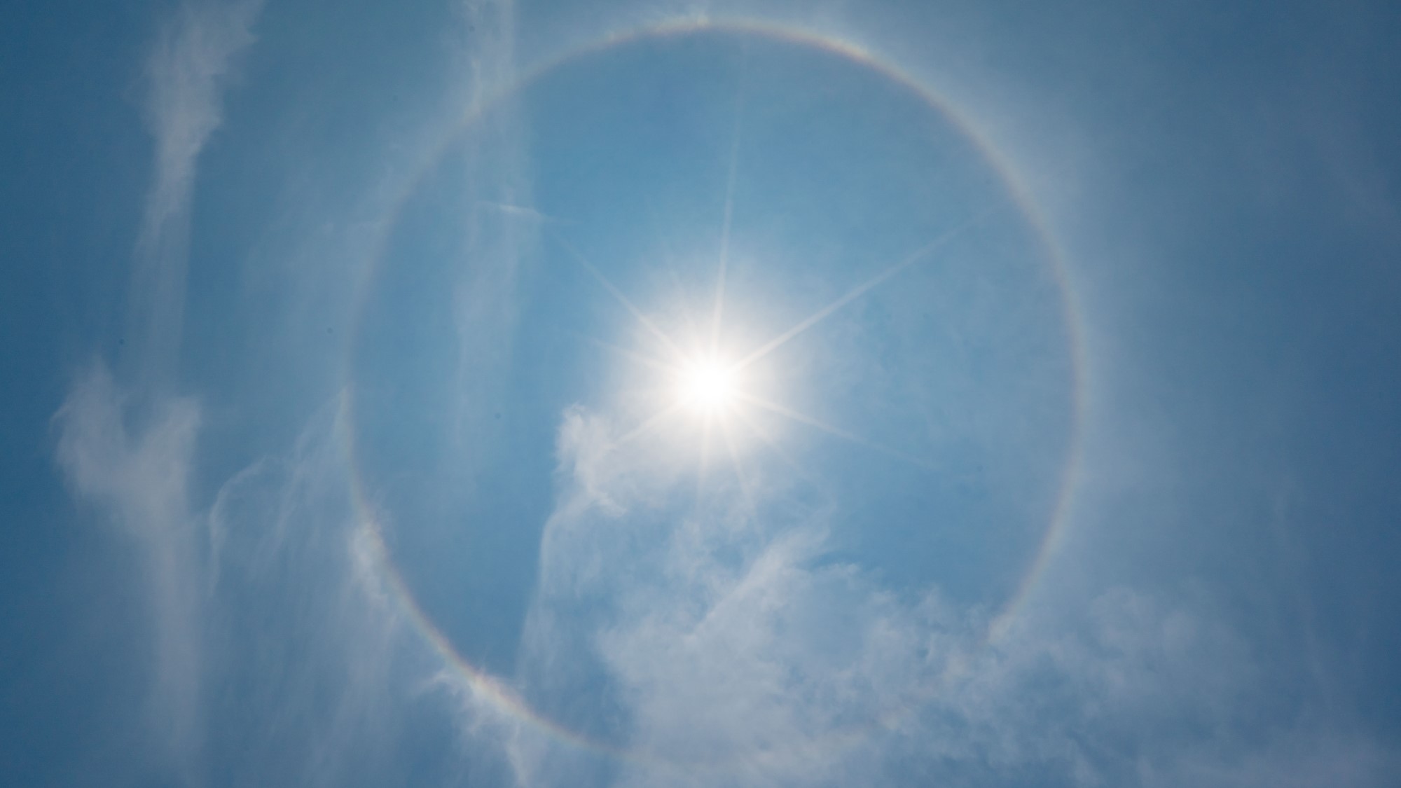 the sun surrounded by a bright ring against a blue sky with wispy white clouds