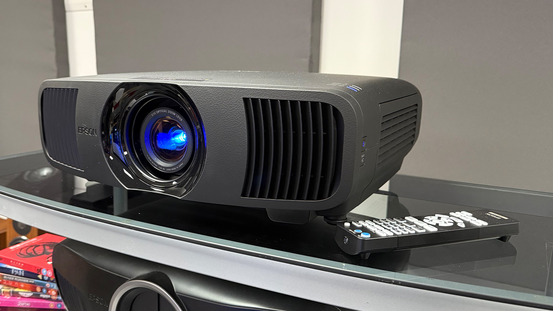 Epson EH-LS9000 home cinema projector with remote control next to it on glass surface