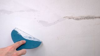 Person fixing crack in white wall with filler and filling knife