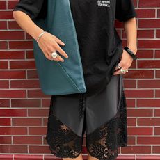 Torivan wears all black outfit, silver accessories, and a teal blue leather tote