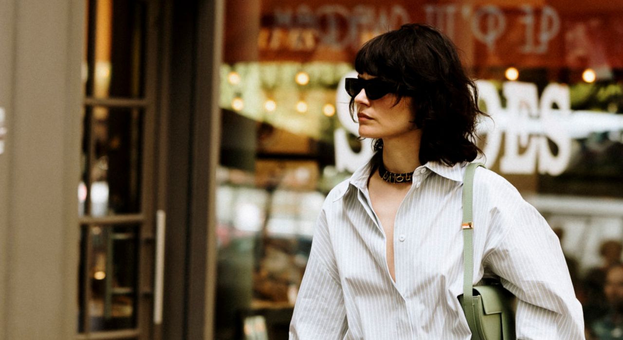 Woman walking down the street in a button-down and a green shoulder bag. 