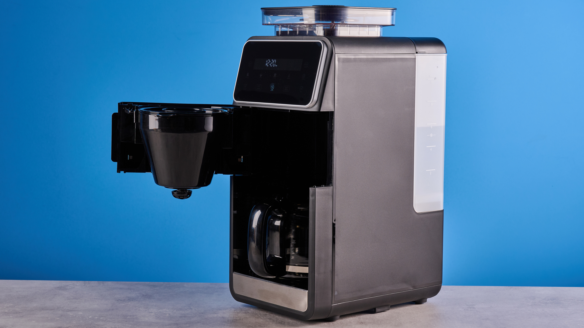 the gevi 10-cup drip coffee maker with grinder photographed against a blue background, showing the glass carafe, water tank, touch screen, and accessories including plastic filter