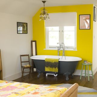 open plan bedroom with yellow wall chandelier and bathtub