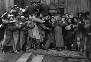 Black and white action shot in Shanghai, China. 1948. Men and women holding on to each other in a pushing crowd, stone steps to the front