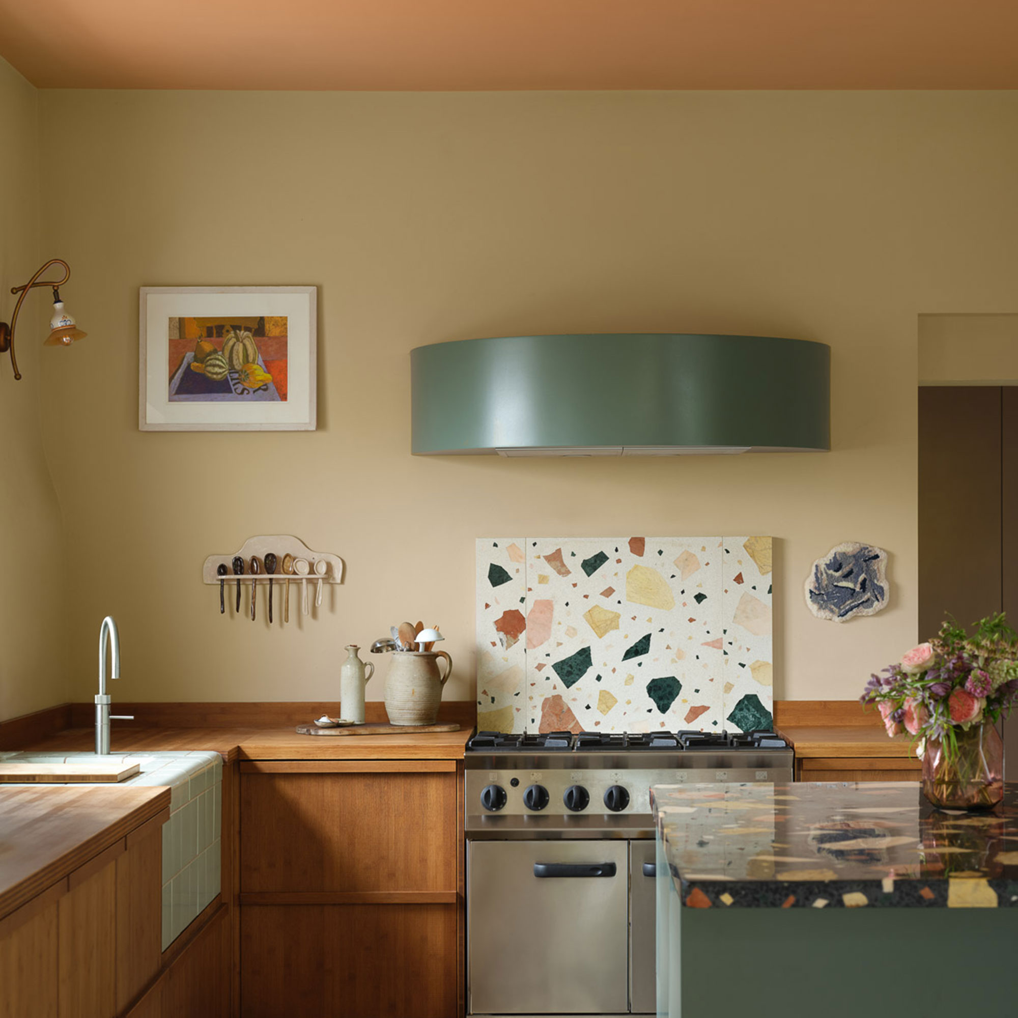 Kitchen with terrazzo splashback, green painted cooker hood, yellow walls and peach ceiling