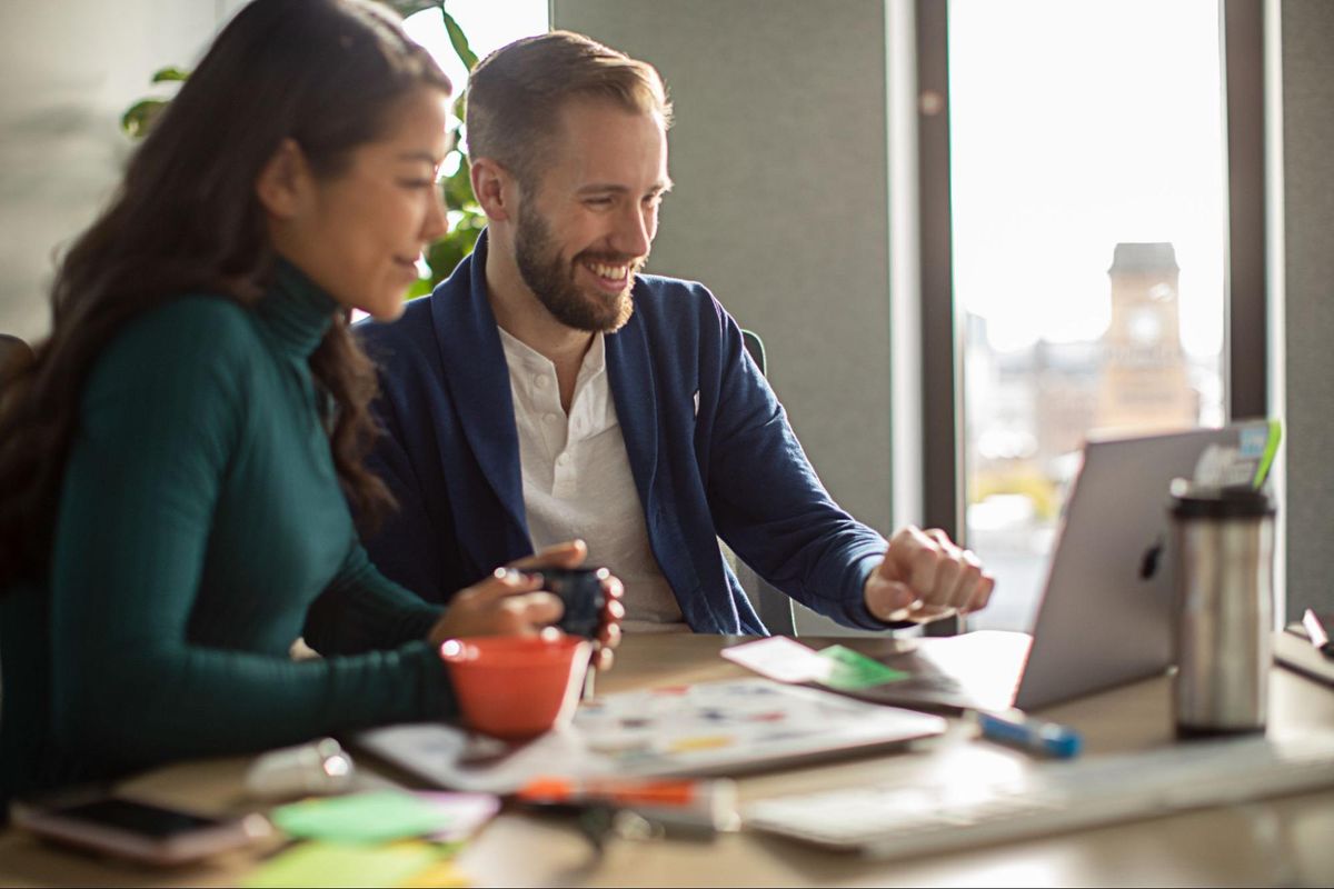 Man and woman smiling while sitting at a desk looking at a computer