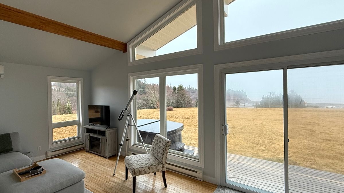 A telescope next to glass windows in a cabin facing the wilderness of Canada