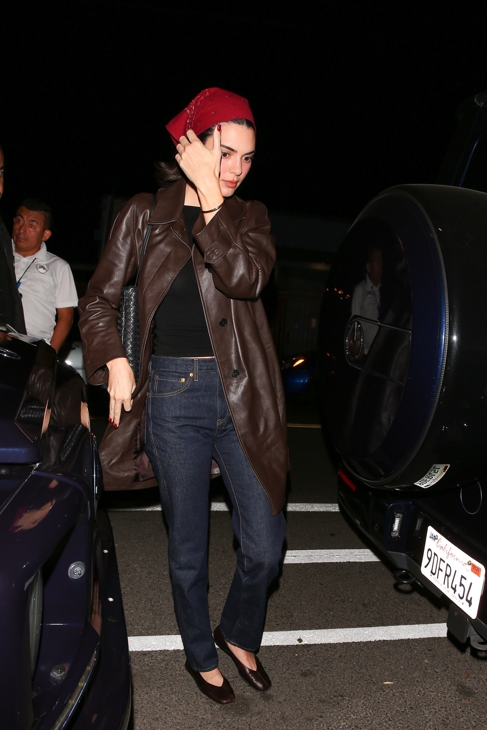 Kendall Jenner wears a red bandana, brown leather jacket, black top, dark-wash jeans, and The Row ballet flats.