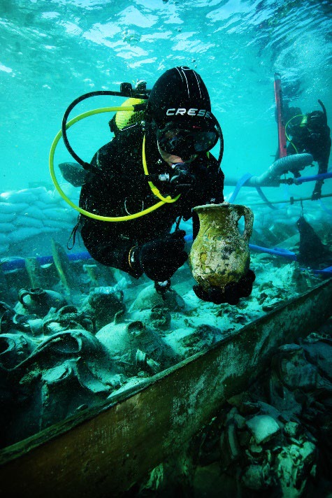 Underwater, a scuba diver holds up a pitcher from the wreck
