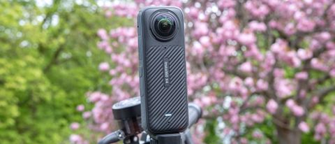 A photo of the Insta360 X4 mounted to motorcycle handlebars with green foliage and a pink blossoming tree in the background