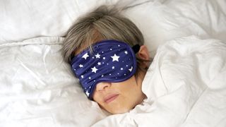 A woman wears a blue sleep mask with white stars while taking a daytime nap in bed