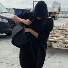 Kendall Jenner wearing a blue cloche hat, The Row bag, black cape, dark-wash cuffed jeans, and black glove flats.