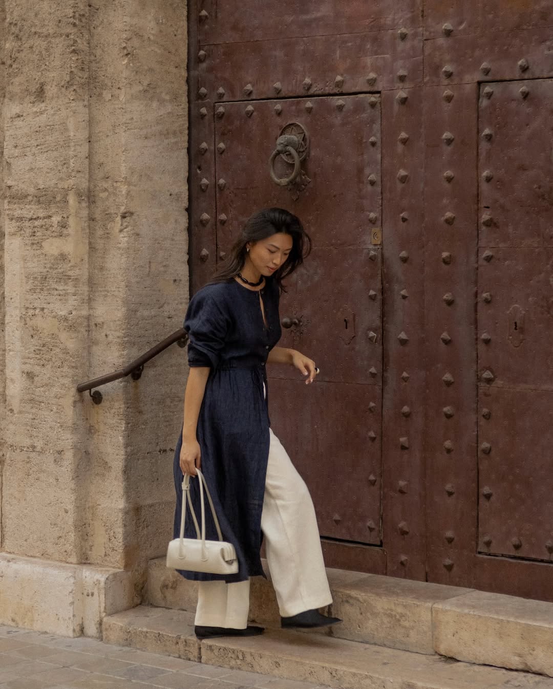 @michellelin.lin wears cream trousers navy dress white bag