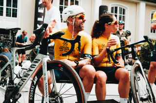 cyclist are seen sitting on a bench holding their bikes