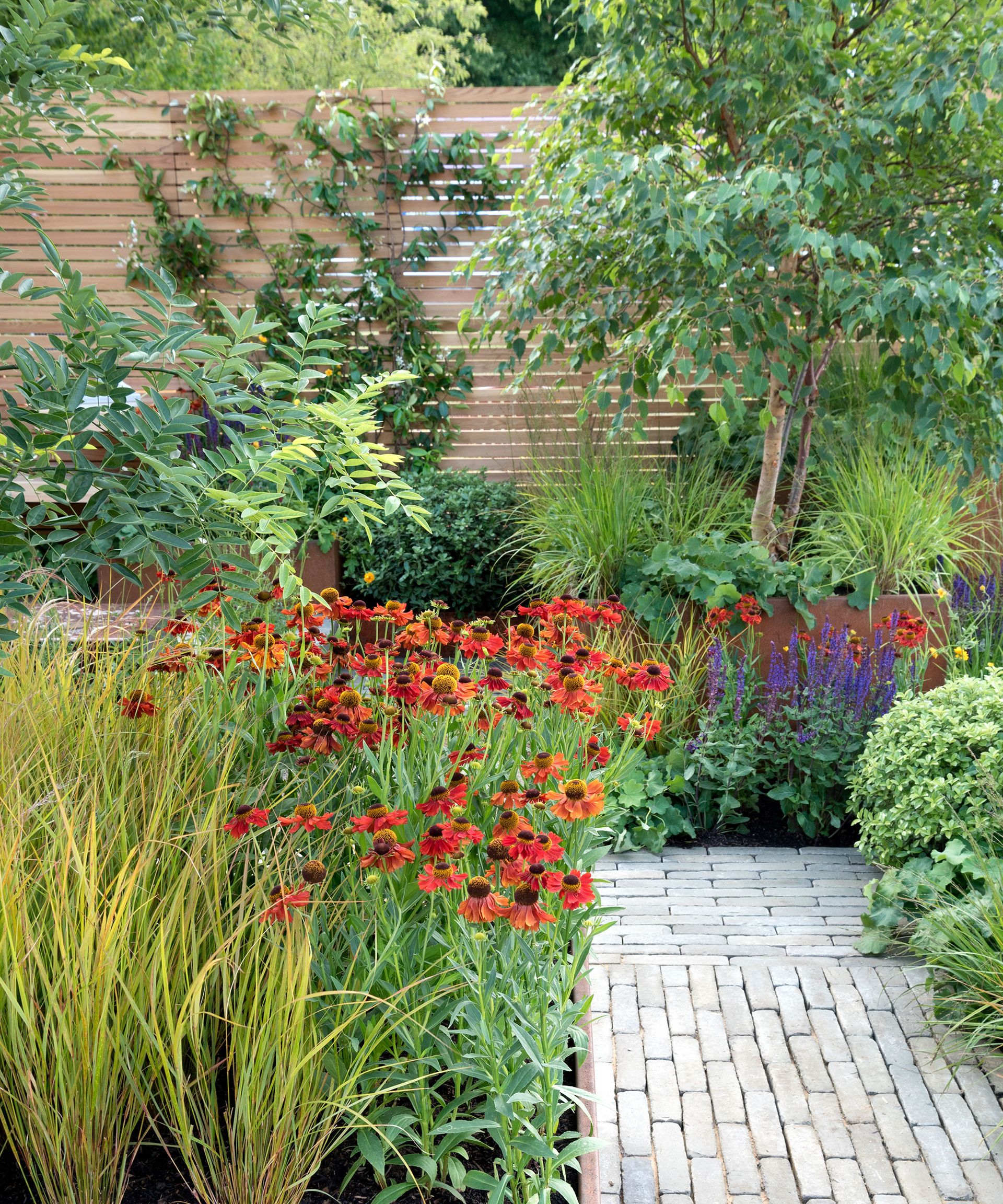 brick pathway through flower beds with a slatted fence at the end of the path
