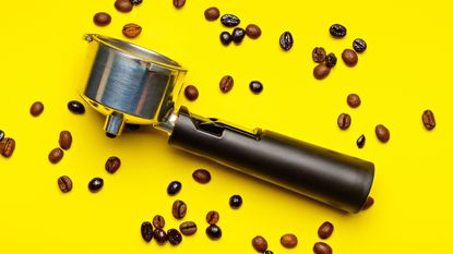 An espresso portafilter on a yellow background with coffee beans
