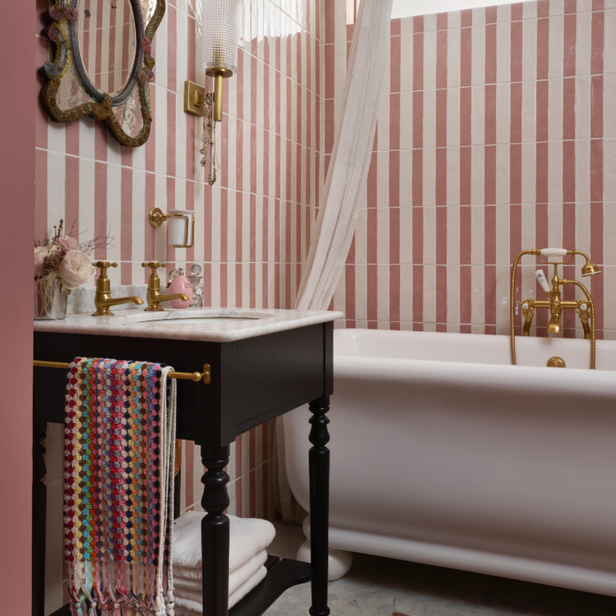 Pearl Lowe's bathroom with pink and white tiles, white freestanding bath, washstand with marble top, patterned towel, vintage mirror
