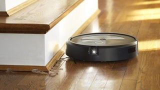 The iRobot Roomba J series AI vacuum by a wood staircase.