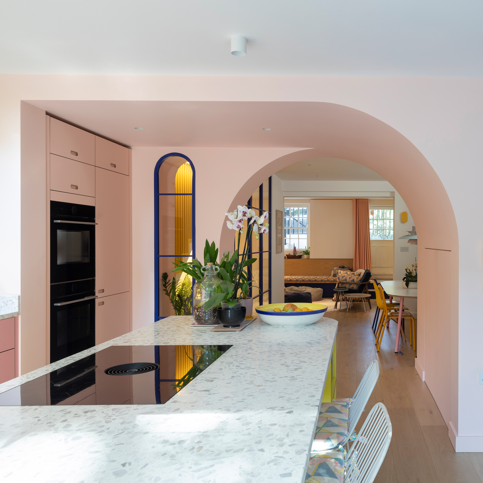 a pink and white open plan kitchen with an arched wall to ceiling