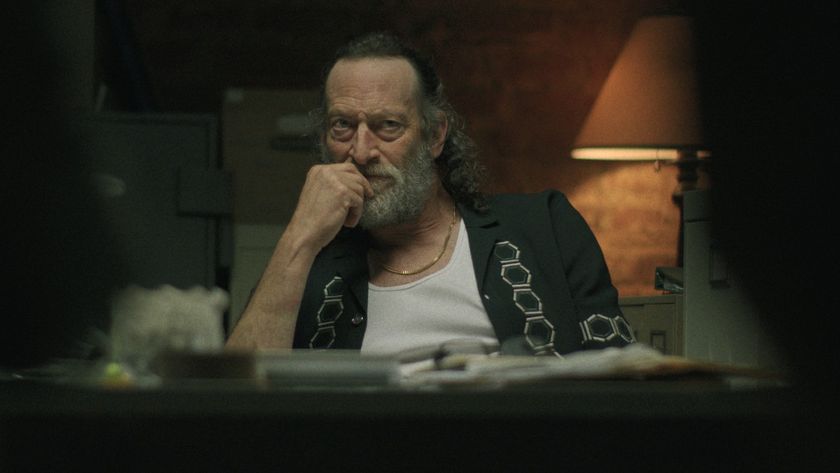 Troy Kotsur in Black Rabbit putting his left hand up to his chin with his elbow resting on the table. 