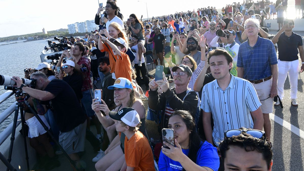 A large crowd of onlookers hold up phones and cameras while craning their necks to watch an event.