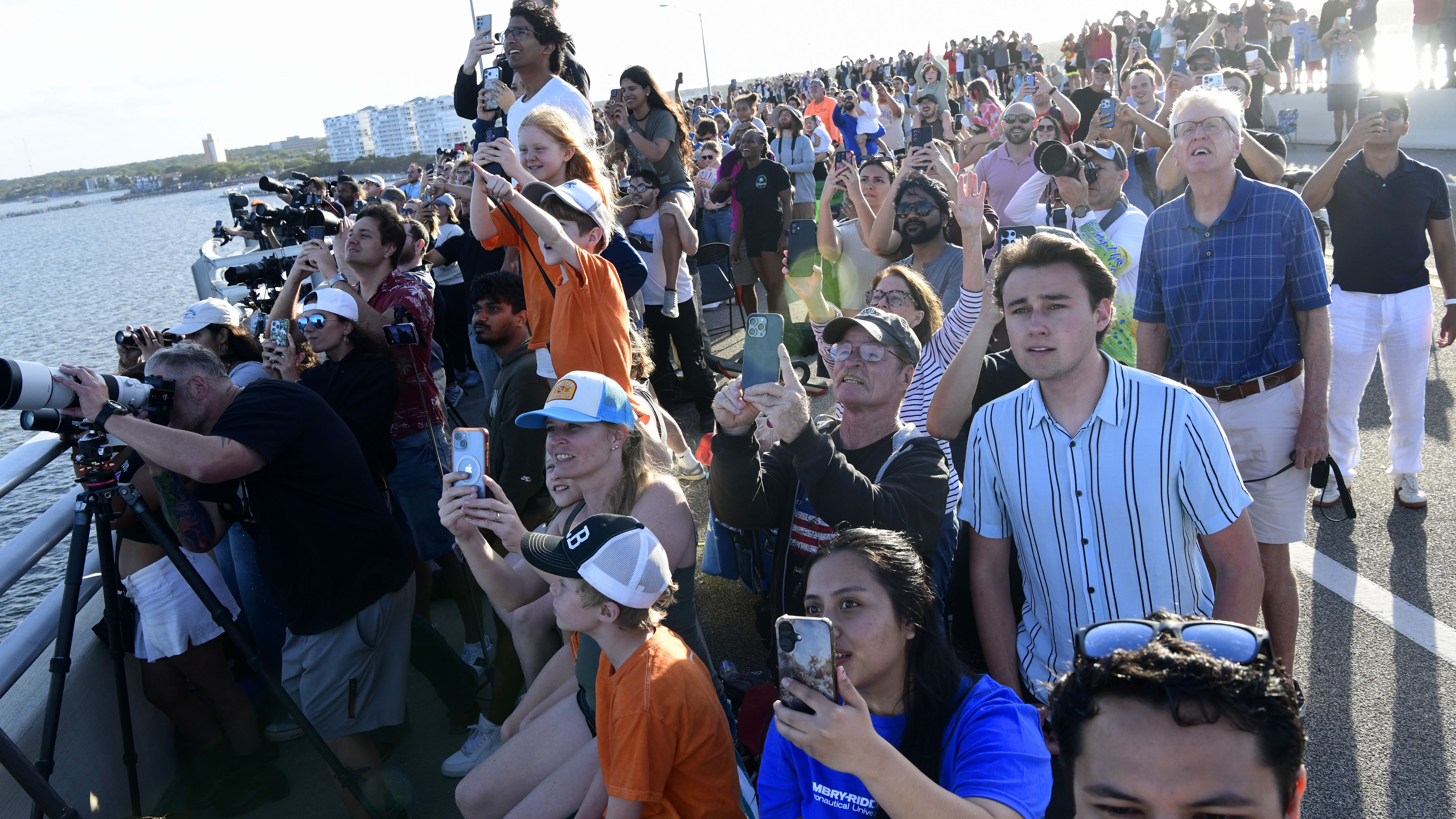 A large crowd of onlookers hold up phones and cameras while craning their necks to watch an event.