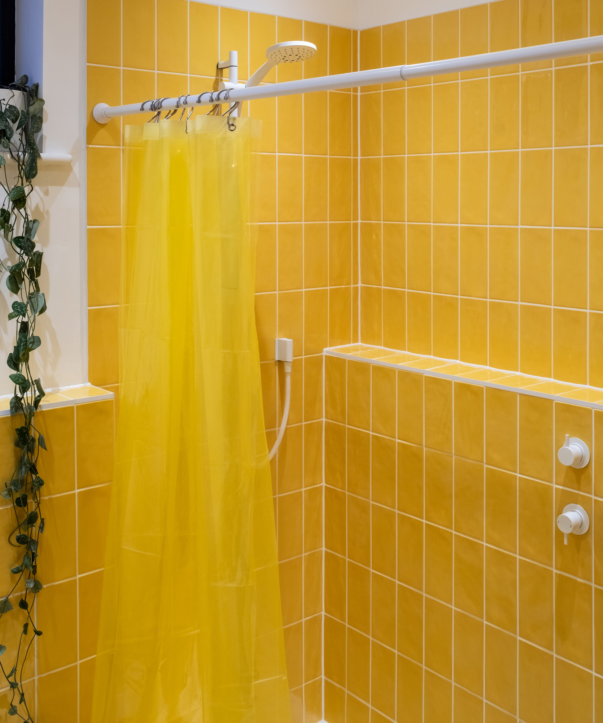 A bright yellow tiled shower with white fixtures creating a modern but retro feel. There is a shower curtain which is also yellow
