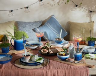 outdoor dining table with rust coloured linen table cloth and bold blue dinnerware