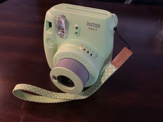 Green Fujifilm Instax Mini 9 on wood table front with angle while camera on