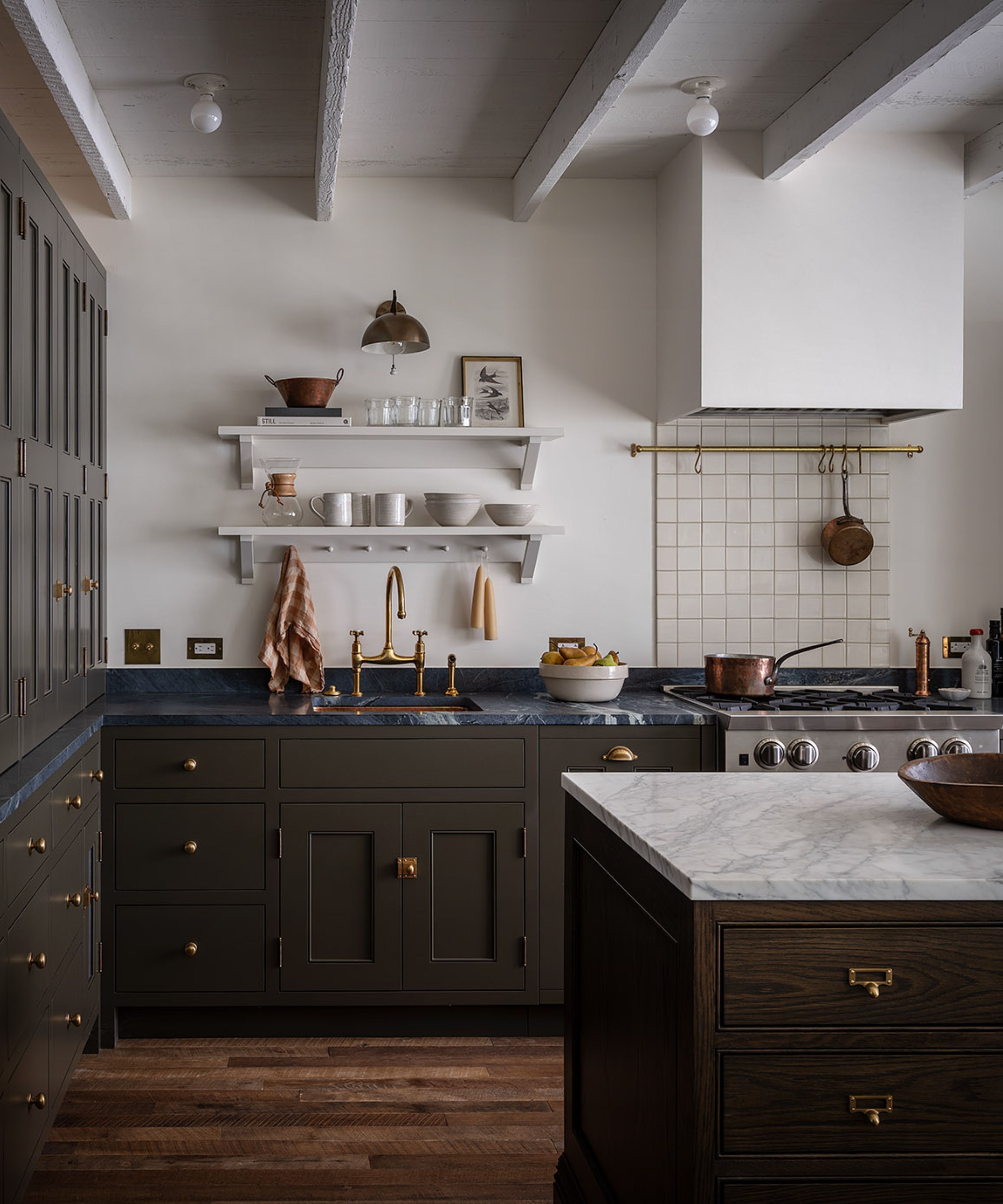 a compact warm industrial kitchen with painted rustic ceiling beams and olive green cabinetry styled with brass hardware and accessories