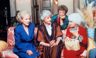 four older women sit on a couch and have a conversation in golden girls