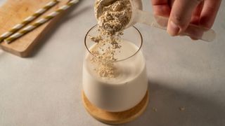 Protein powder being scooped into glass with milk