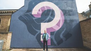 A photo of web typography expert Richard Rutter standing in front of a wall on which a street artist has painted a giant mauve question mark.