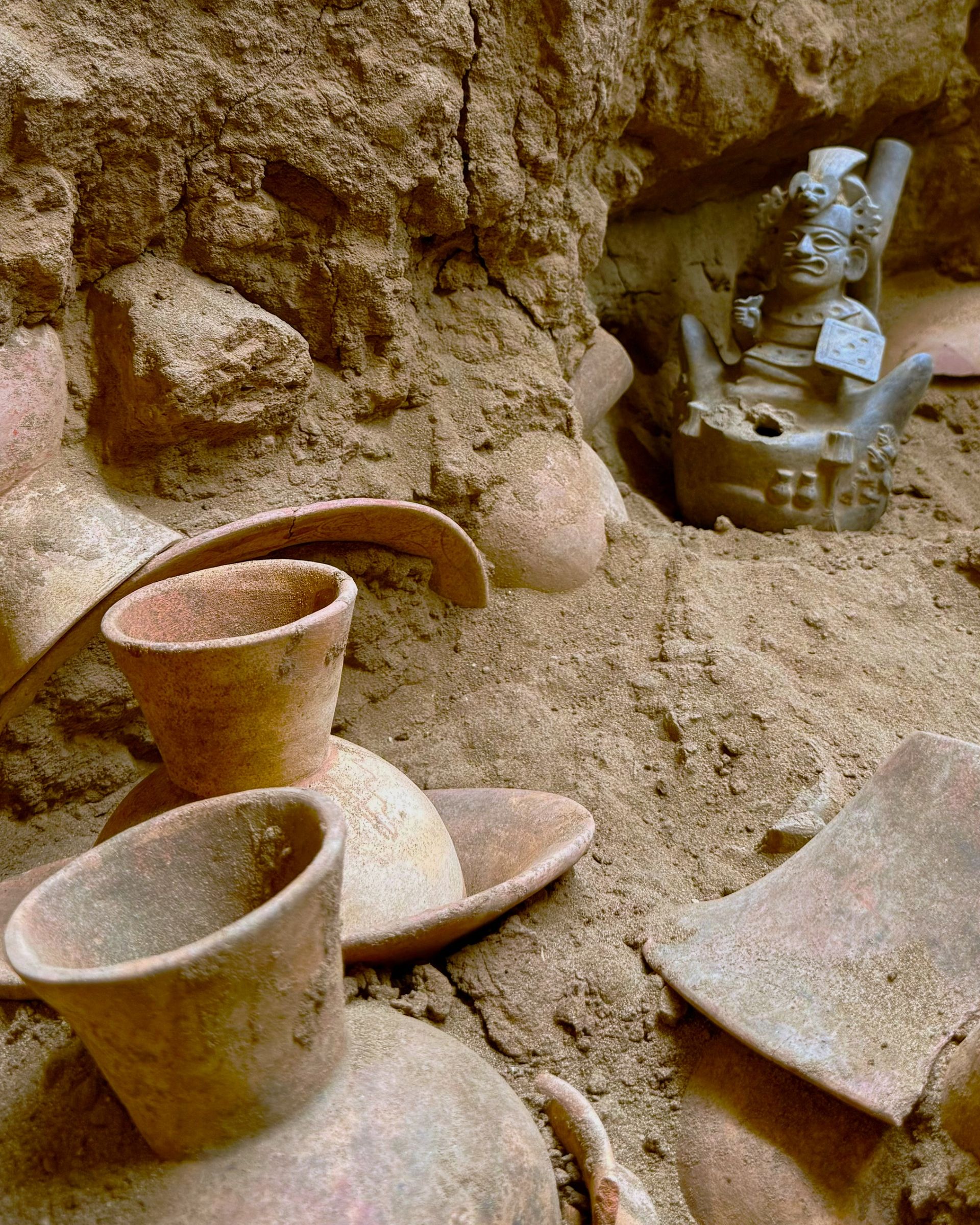 A series of ceramic bowls and vases are half unearthed in a cave.