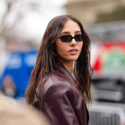 Yasmin Wijnaldum wears black sunglasses, burgundy bordeaux belted leather trench coat, outside Zimmermann, during the Paris Fashion week Women's Fall/Winter 2025-2026 on March 10, 2025 in Paris, France.