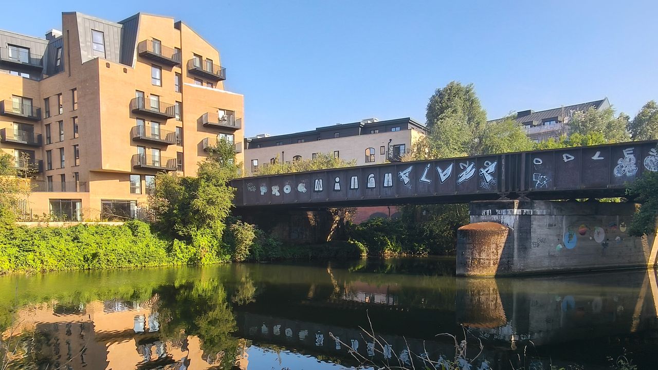 A bridge, apartment building and blue sky reflected in a river.