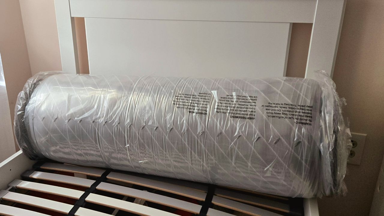 Siena Premier Hybrid Mattress rolled in plastic and placed on a slatted bed base with a white headboard