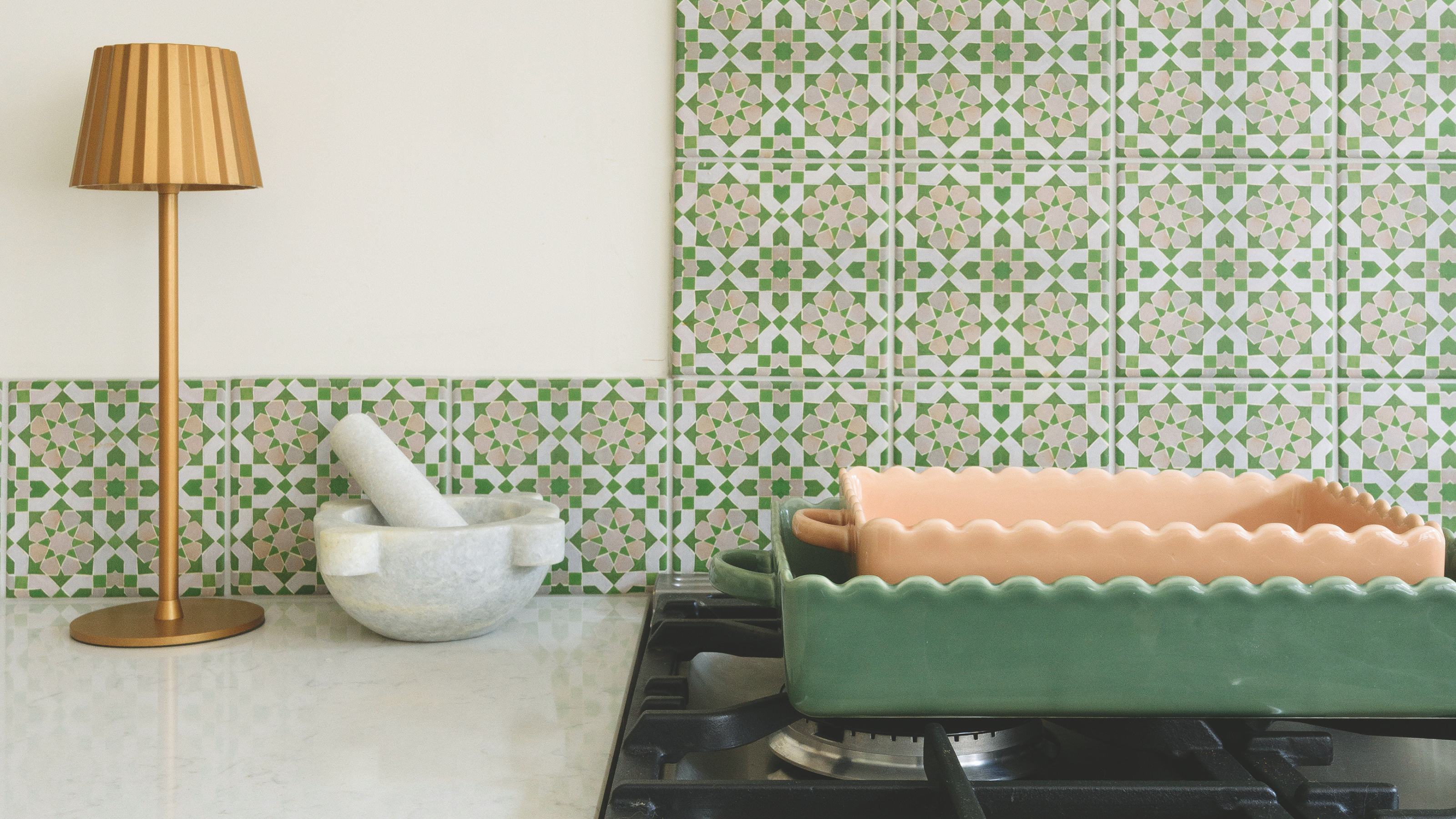 Two ceramic baking dishes on an oven. One is pink and the other is green.